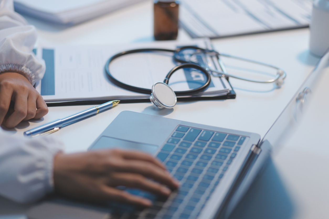 A professional and focused Asian female doctor in scrubs is working and reading medical research on her laptop in her office at a hospital. healthcare-fraud-defense-lawyer